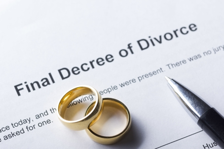 Two gold wedding bands and a pen sit on top of a Final Decree of Divorce